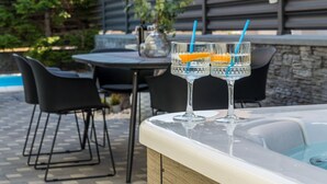 A poolside area with a hot tub, two glasses with orange slices, and a table with chairs.