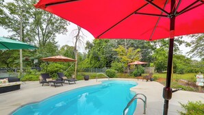 Ein Pool mit Liegestühlen und Sonnenschirmen, umgeben von Grün.