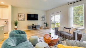 Ein modernes Wohnzimmer mit einer Couch, Poufs, einem Couchtisch und einem Fernseher.