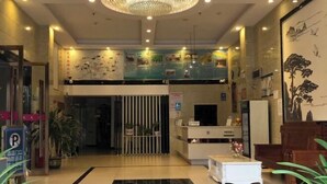 Un vestíbulo de hotel con mostrador de recepción, piso a cuadros en blanco y negro y una gran araña.