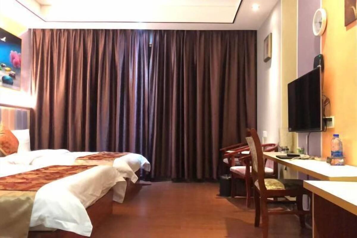 Una habitación de hotel con dos camas, un escritorio, una silla, un televisor y una cortina.