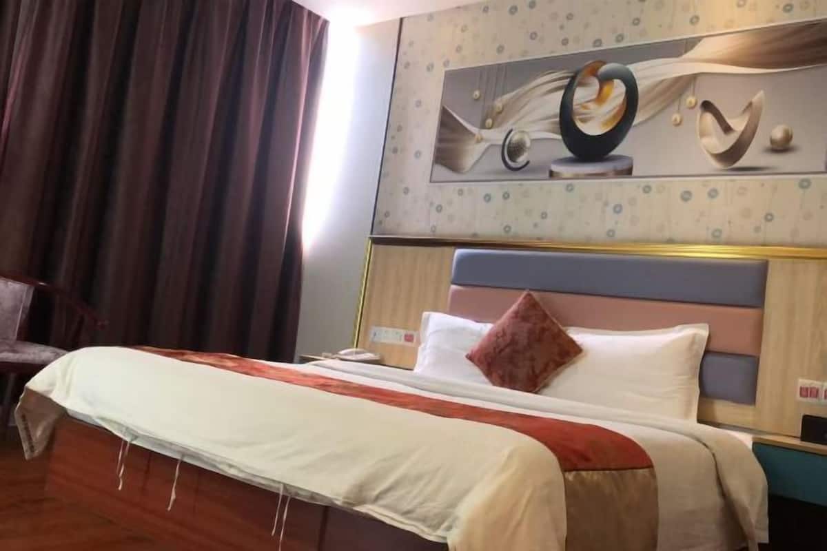 Una habitación de hotel con una cama, cabecera, una obra de arte en la pared y una cortina.