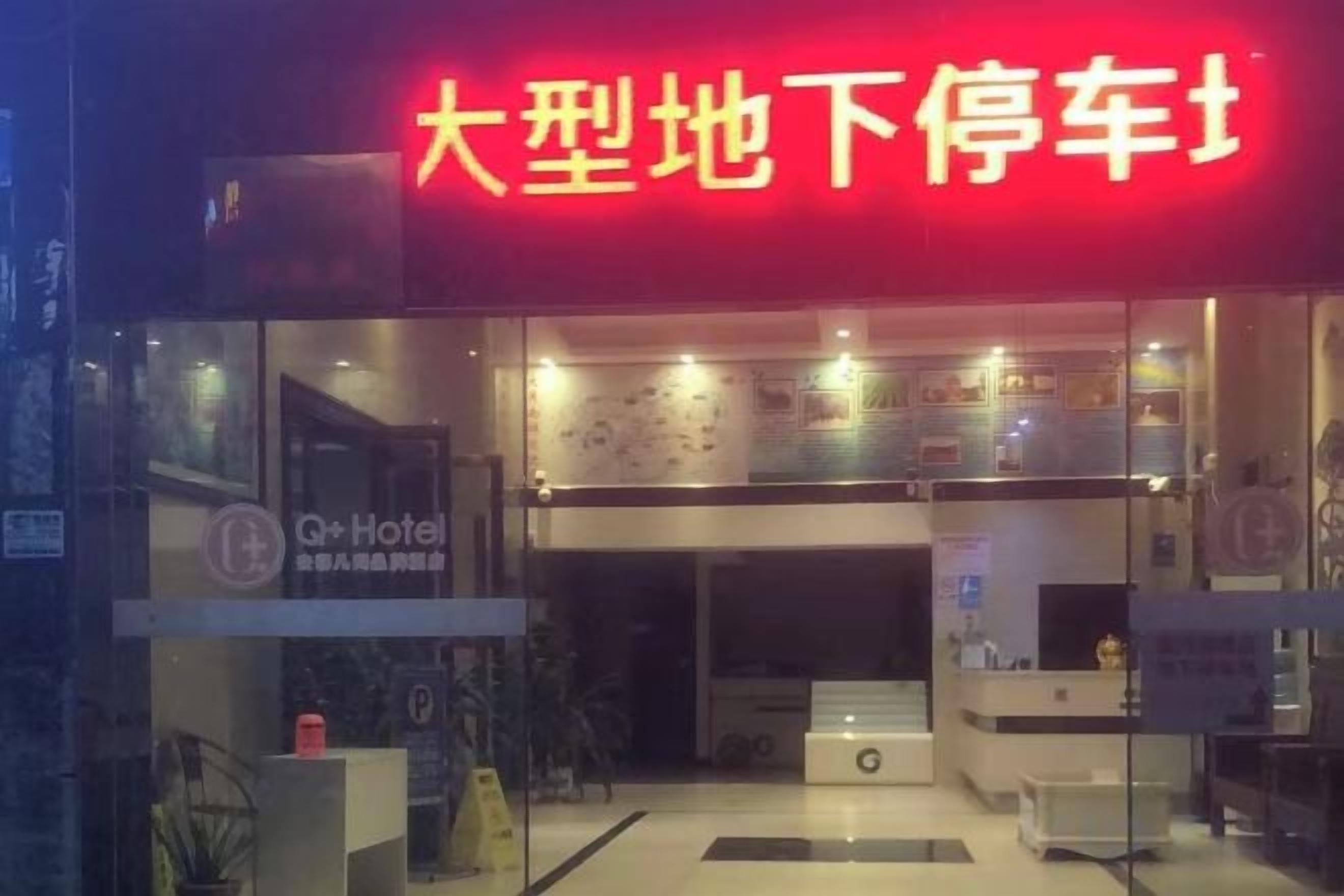 A hotel entrance with a red sign, a reception desk, and a glass facade.