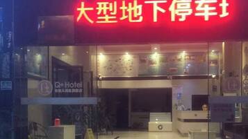 A hotel entrance with a red sign, a reception desk, and a glass facade.
