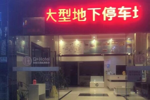A hotel entrance with a red sign, a reception desk, and a glass facade.