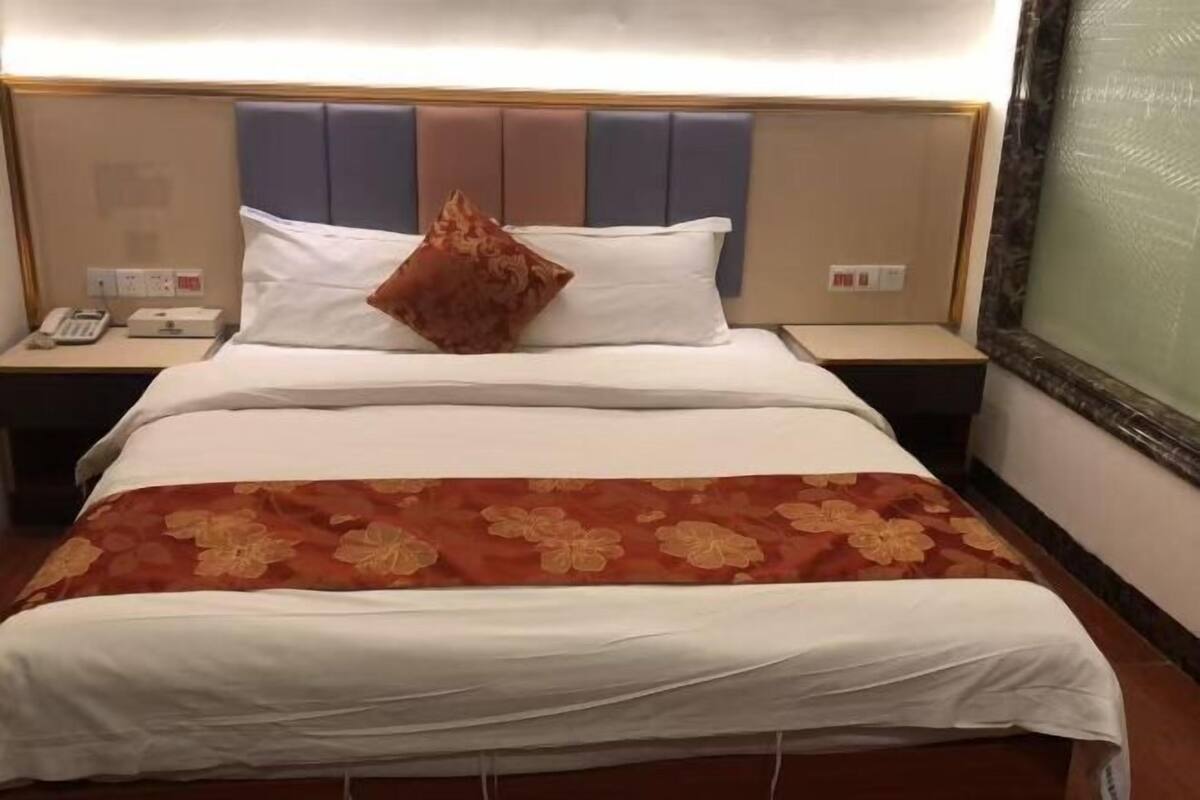 Habitación de hotel con una cama, una mesita de noche, un teléfono y un panel de control en la pared.