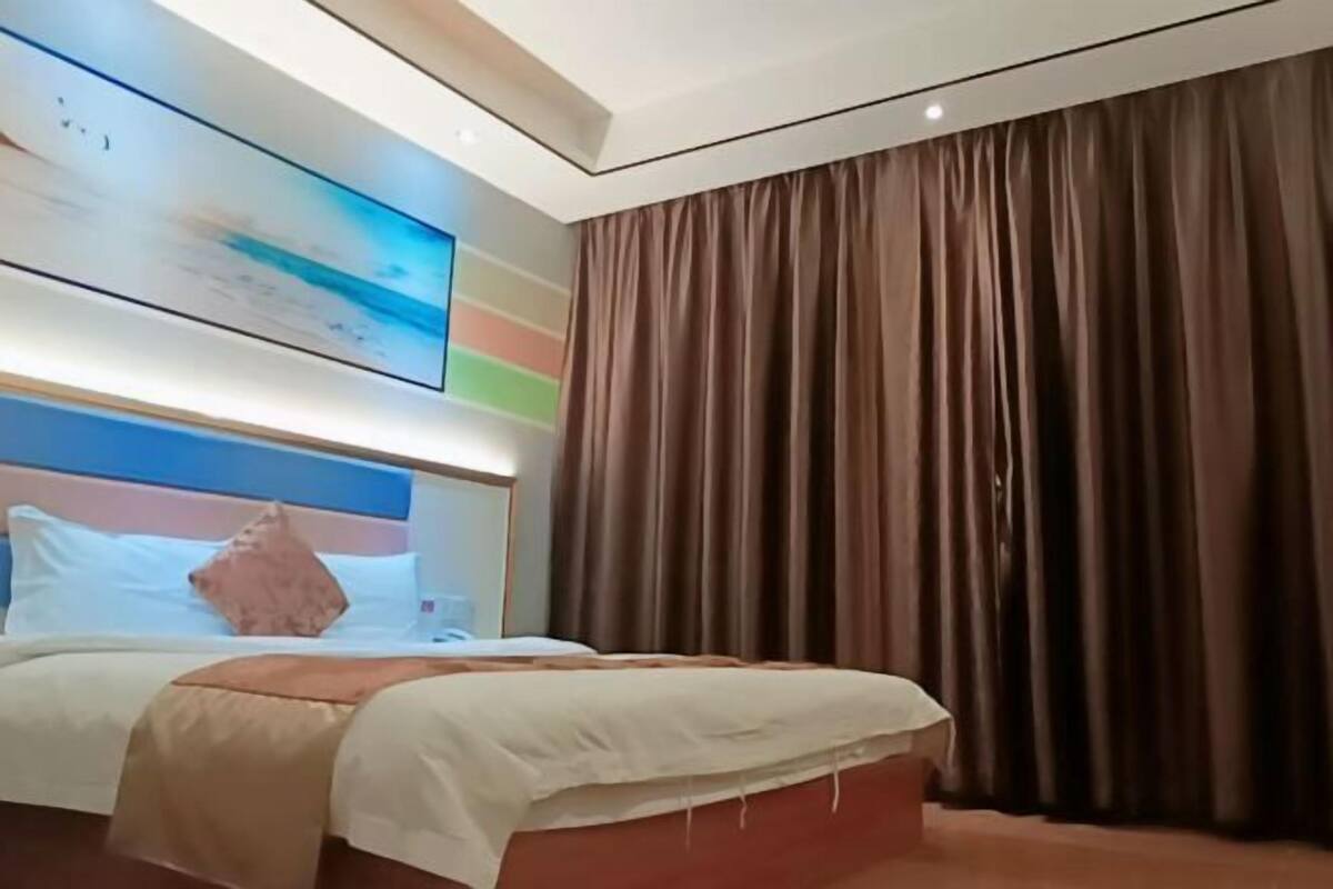 Una habitación de hotel moderna con una cama grande, un cabecero con diseño colorido, un ventanal con cortinas y una obra de arte colgada en la pared.