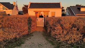 Une maison avec une entrée fermée par un portail, entourée de broussailles sèches, et un ciel dégagé.