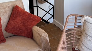 Un salon avec un canapé beige, un fauteuil en osier et un escalier menant à un niveau supérieur.