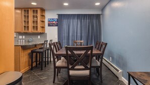 A dining area with a wooden table and chairs, a kitchen with wooden cabinets, and a blue wall. - Cozy City Stay - 3bdrm near Airport (Anchorage)