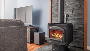 A modern living room with a stone wall, a black wood-burning stove, a sofa, and a TV. - Cozy City Stay - 3bdrm near Airport (Anchorage)
