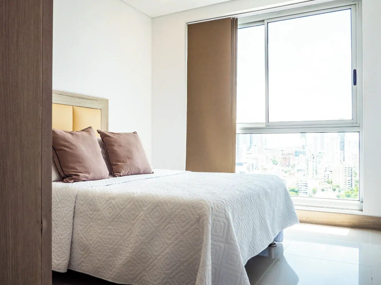 A modern bedroom with a large window, a bed with a quilted cover, and two pillows.