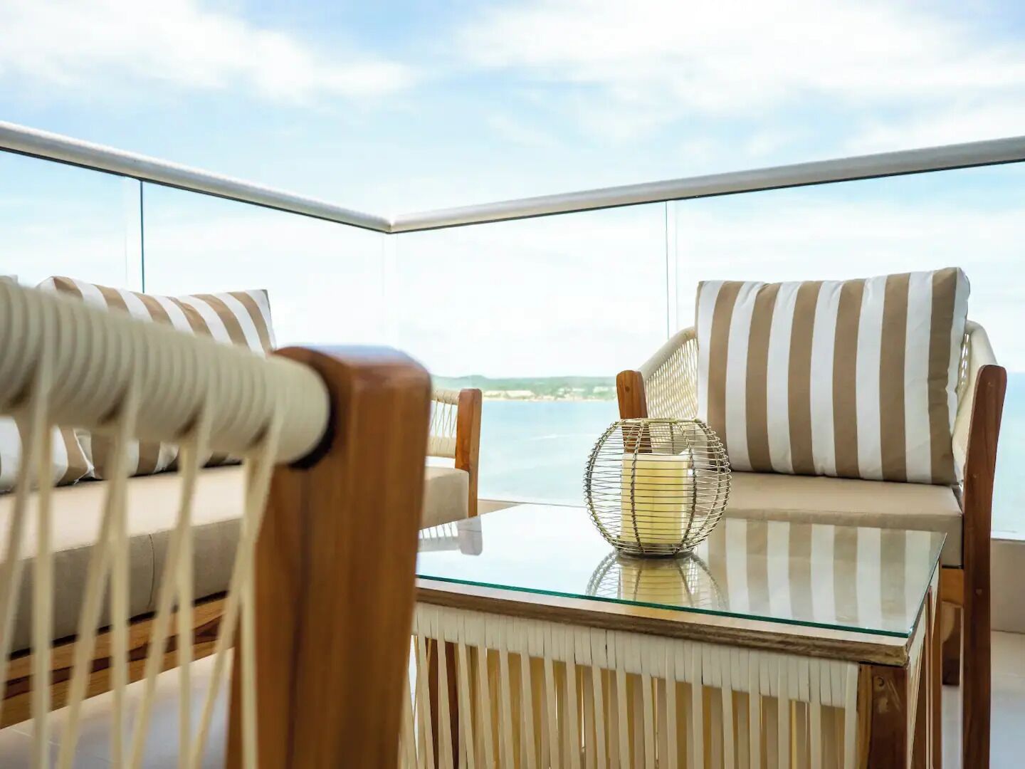 A balcony with two striped chairs, a glass table, and a wire basket.