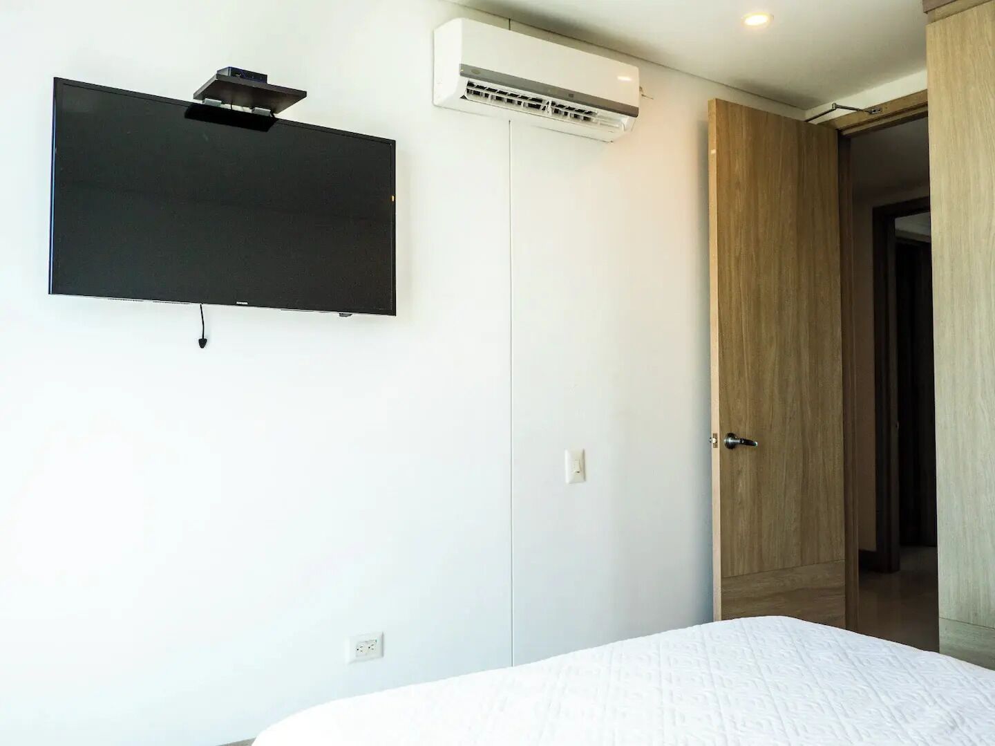 Une chambre à coucher comprenant un lit, un téléviseur à écran plat fixé au mur, une armoire blanche et un appareil de climatisation.