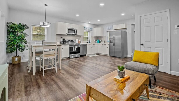 Une cuisine moderne avec des meubles blancs, des appareils en acier inoxydable et un coin repas comprenant une table et des chaises en bois.