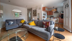 A modern living room with a grey sofa, a glass coffee table, and a dining area with a white table and chairs.