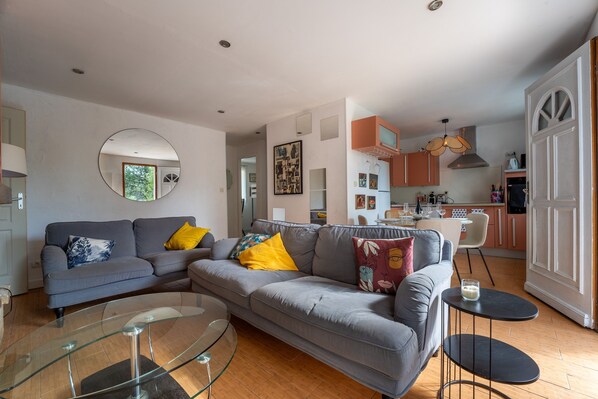 A modern living room with a grey sofa, a glass coffee table, and a dining area with a white table and chairs.