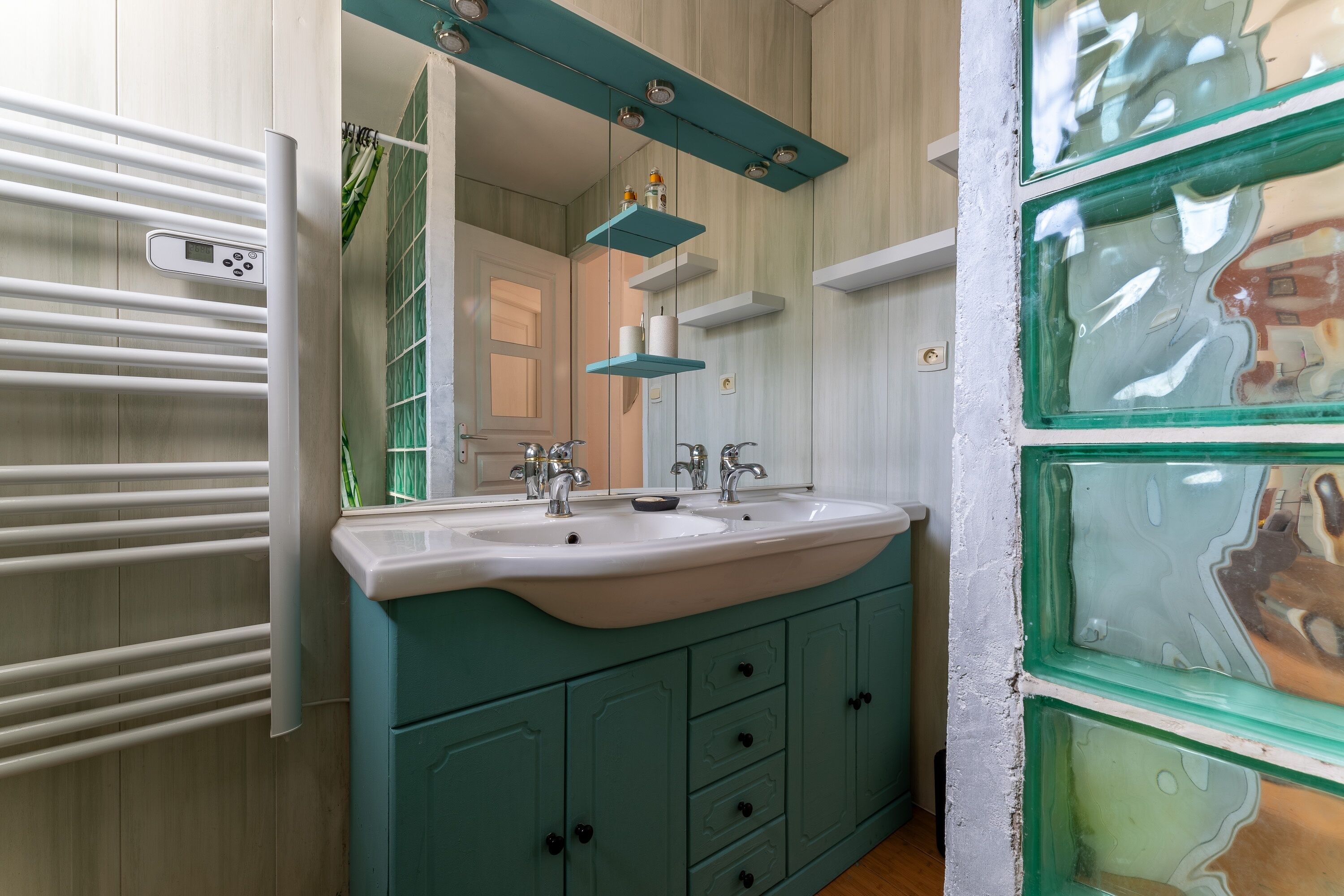 A bathroom with a white sink, teal cabinets, and a mirror with a teal shelf above it.
