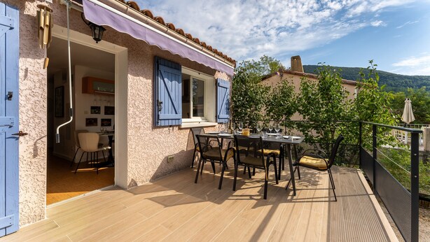 A patio with a table and chairs, a blue door, and a view of a mountain. - Le Martinet - Maison avec piscine (Robiac-Rochessadoule)