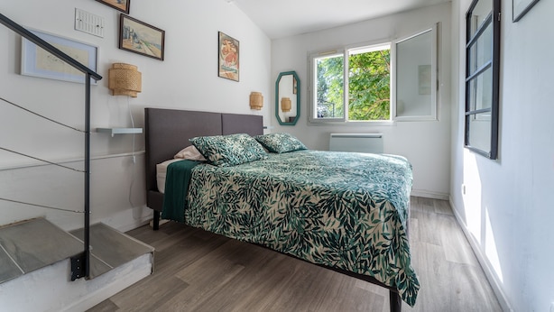 A bedroom with a bed, a staircase, a window, and wall-mounted artwork.