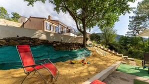A sandy outdoor area with a red chair, a red container, and a green tarp.