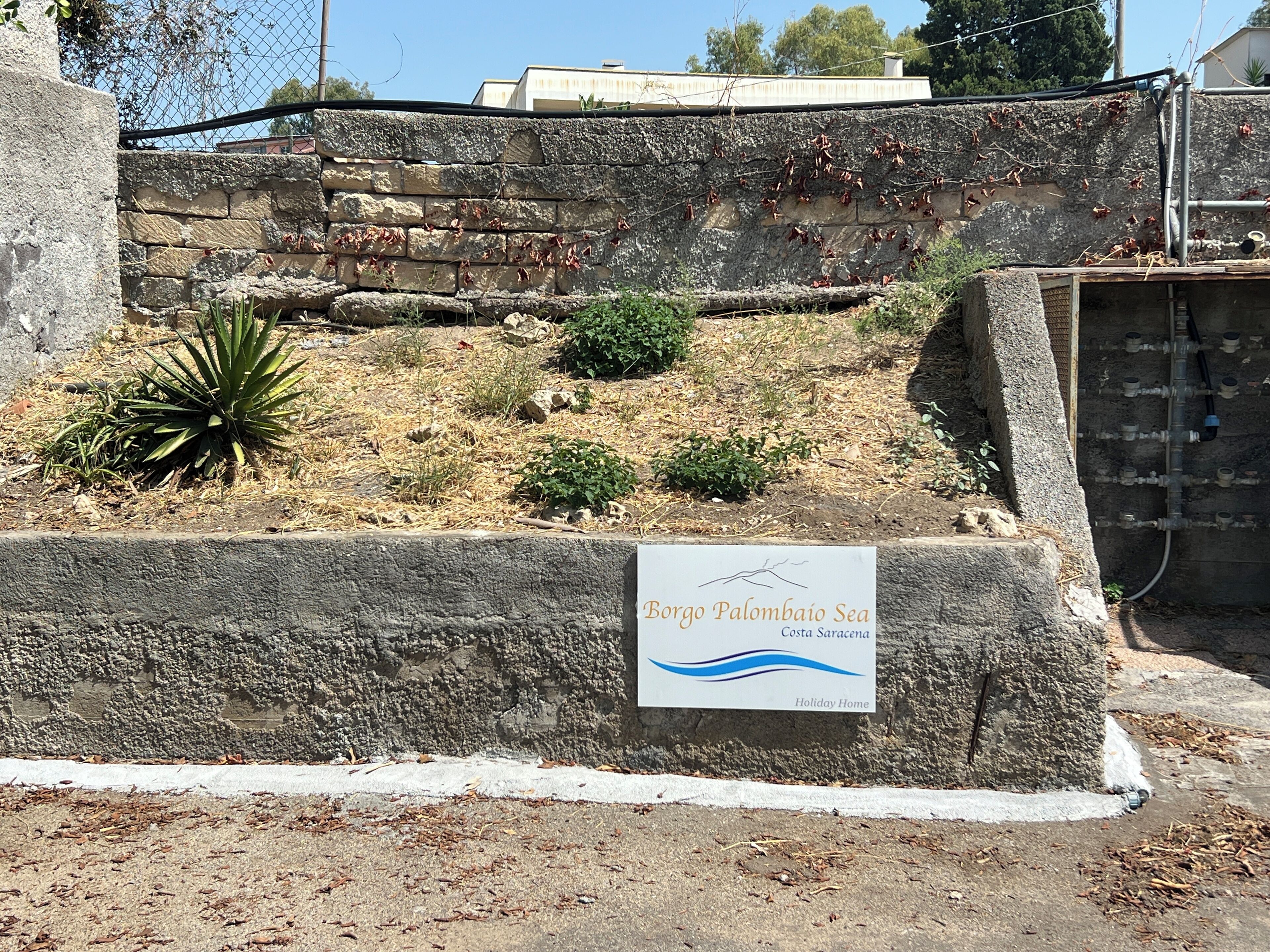 Un mur de pierre sur lequel est apposée une plaque indiquant : « Borgo Palombaio, résidence de vacances en bord de mer, Costa Sarsena ».