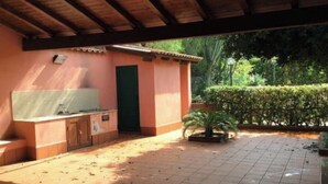 Zona de pati exterior amb terra de rajola, una taula petita i una porta verda.