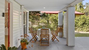 A covered patio with a round table and six wooden chairs, surrounded by a garden. - Time to Drift, Time to Reset (BEACHMERE)