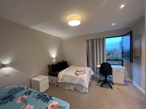 A modern bedroom with a bed, bedside tables, a desk, and a chair. There is a window with a city view. - The Charm view London (Londres)