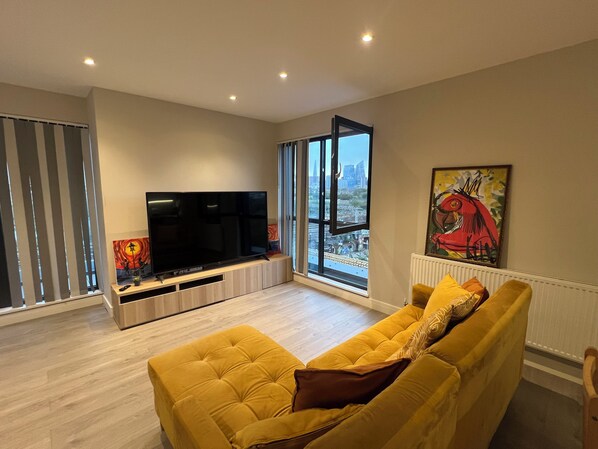 A modern living room with a large flat-screen TV, a yellow sofa, and a city view through large windows. - The Charm view London (Londres)