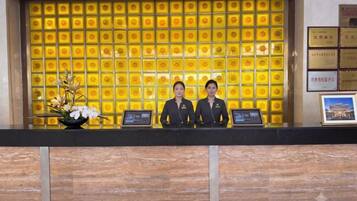 A reception desk with two staff members, a yellow patterned wall, and a framed picture on the wall.