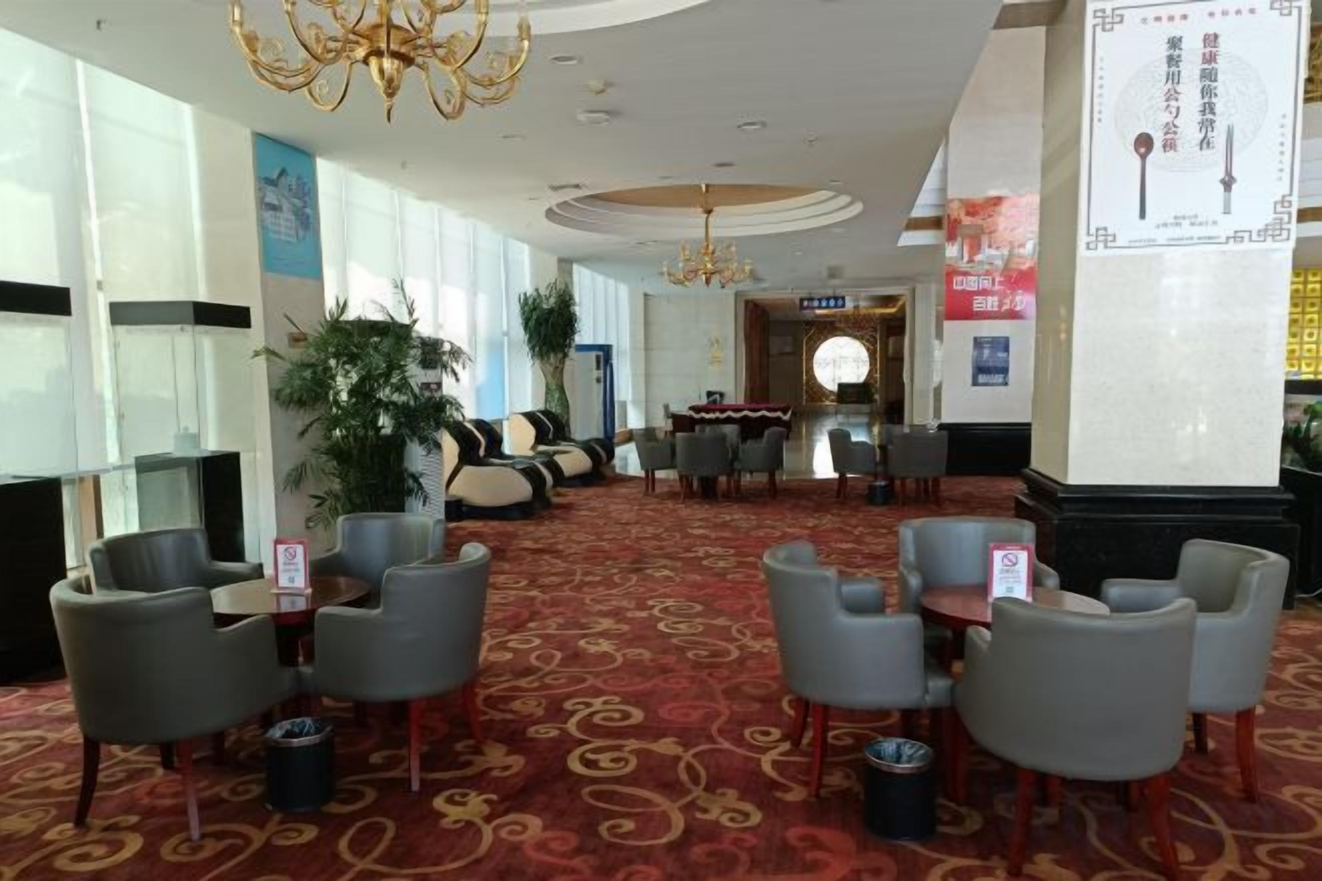 A hotel lobby with a red carpet, seating area with chairs, a chandelier, and a reception desk.