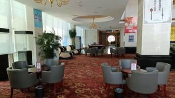A hotel lobby with a red carpet, seating area with chairs, a chandelier, and a reception desk.