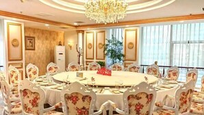 A round dining table with floral chairs, a chandelier, and a large window with curtains. - Tianrui Zhongzhou International Hotel (Ruzhou)