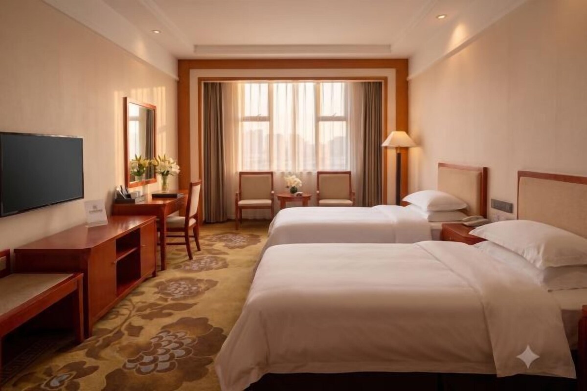 Une chambre d’hôtel avec deux lits, un bureau, une télévision et une grande fenêtre avec des rideaux.