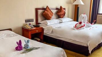 Ein Hotelzimmer mit zwei Betten, jeweils mit weißer Bettwäsche und braunen Kissen. Auf den Betten liegen dekorative Elemente, darunter eine Handtuchskulptur und eine kleine Hasenfigur. Ein Nachttisch mit Telefon und Lampe ist zu sehen.