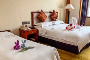 Habitación de hotel con dos camas, cada una con sábanas blancas y almohadas marrones. Se observan elementos decorativos sobre las camas, incluyendo una escultura de toalla y una pequeña figura de conejo. Se aprecia un mesita de noche con un teléfono y una lámpara.