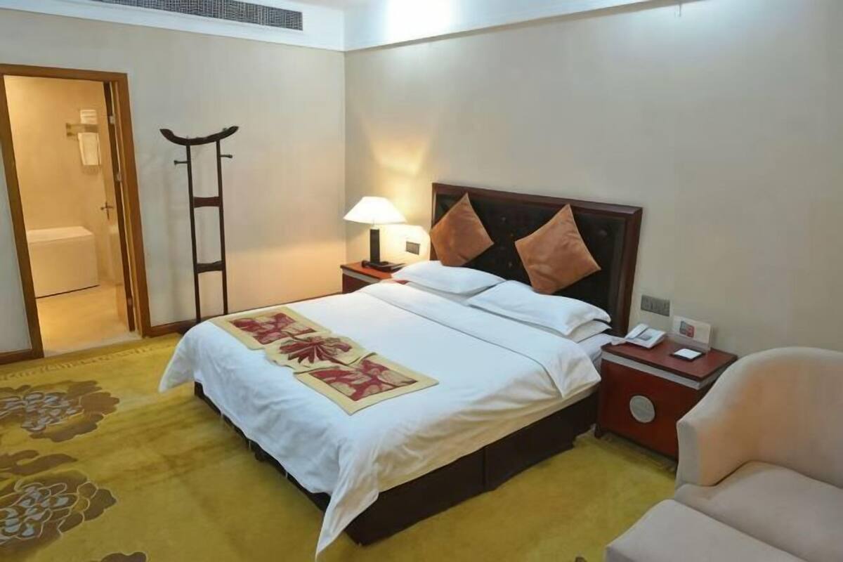 A hotel room with a bed, nightstand, lamp, chair, and a door leading to a bathroom.