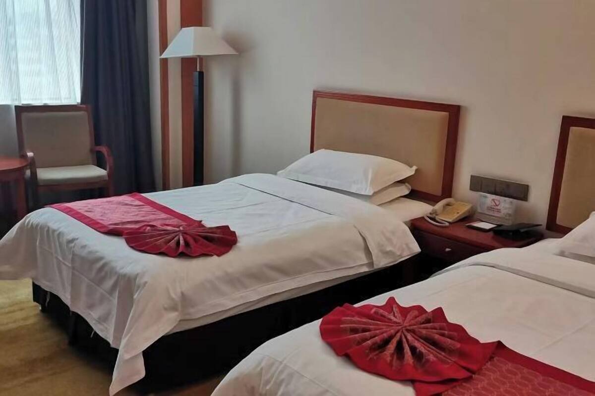 A hotel room with two beds, a chair, a lamp, a phone, and a sign.