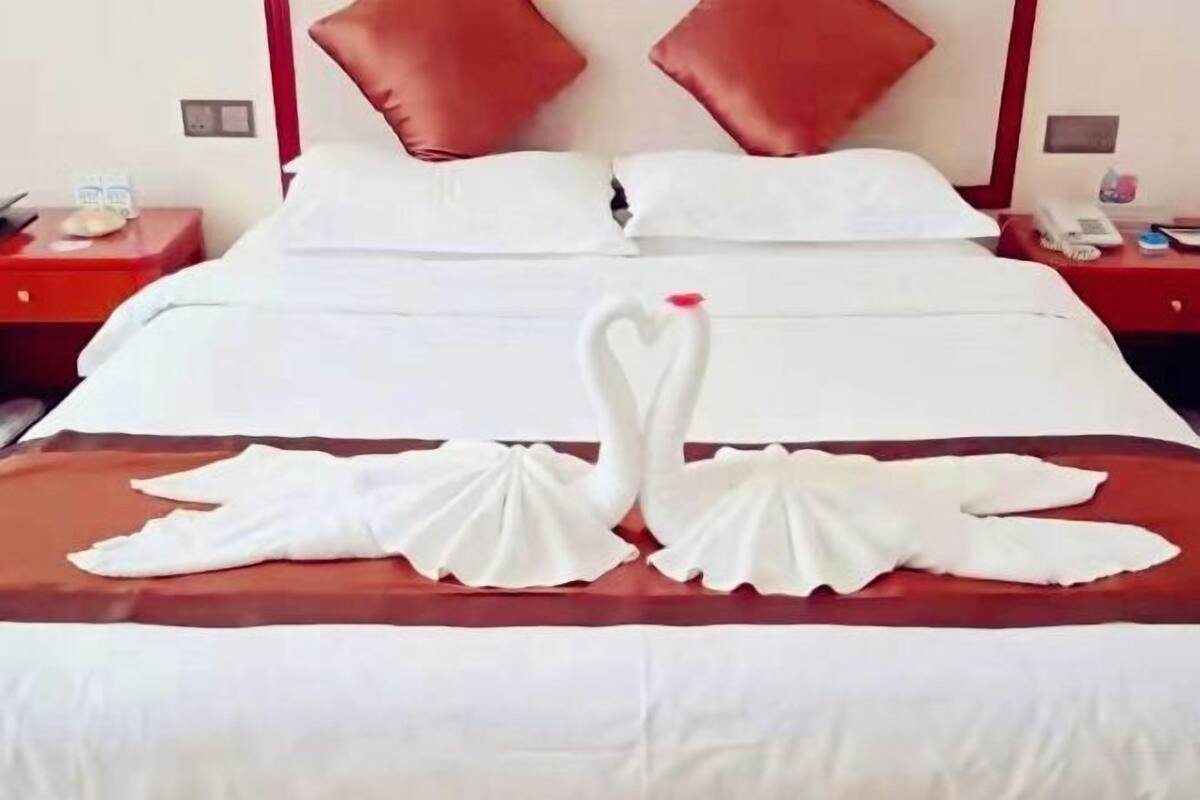 A hotel room with a bed, red nightstands, and a red and white pillow arrangement.