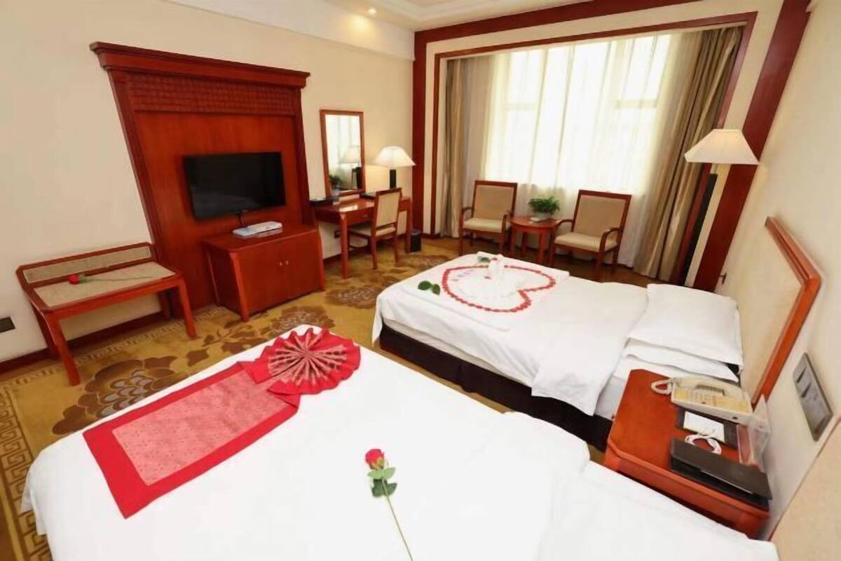 A hotel room with a bed, a desk, a TV, and a window with curtains.