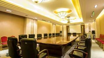A conference room with a long table and chairs, equipped with a projector and a screen.