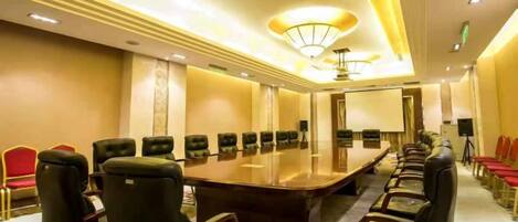 A conference room with a long table and chairs, equipped with a projector and a screen.