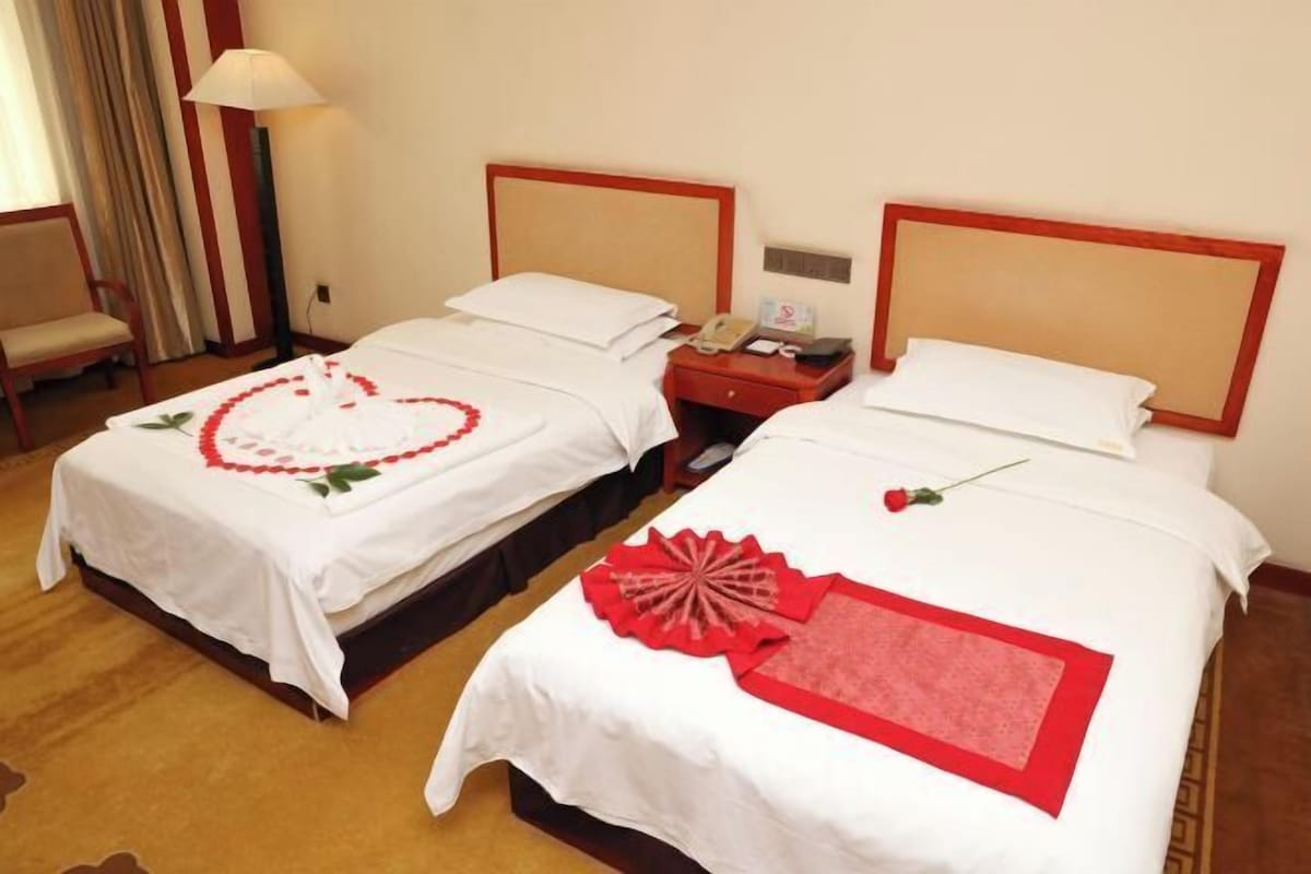 Two single beds with wooden headboards, a bedside table with a lamp, and a chair.