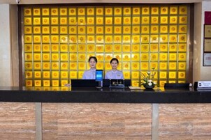 Una reception con due membri dello staff, un display digitale e una parete decorativa con un motivo.