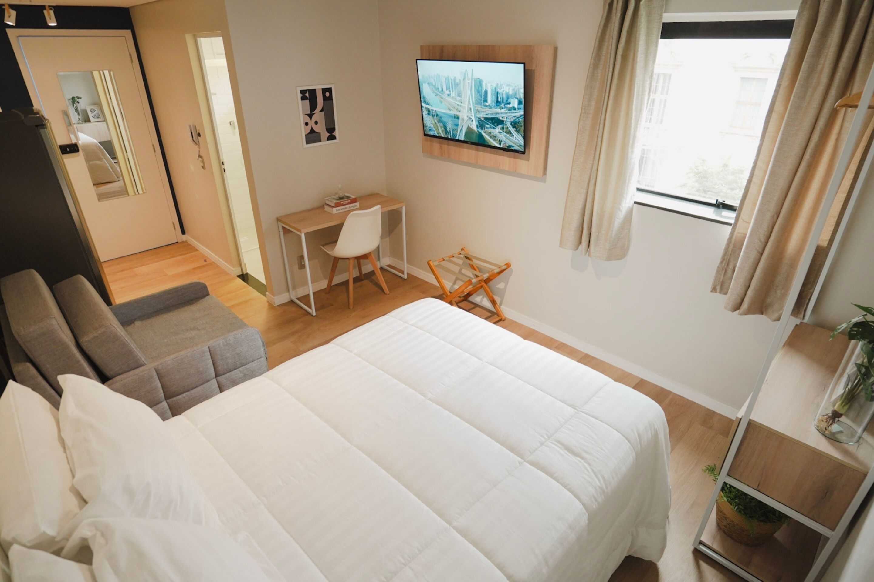 A hotel room with a bed, a desk, a chair, a TV, and a window with curtains.