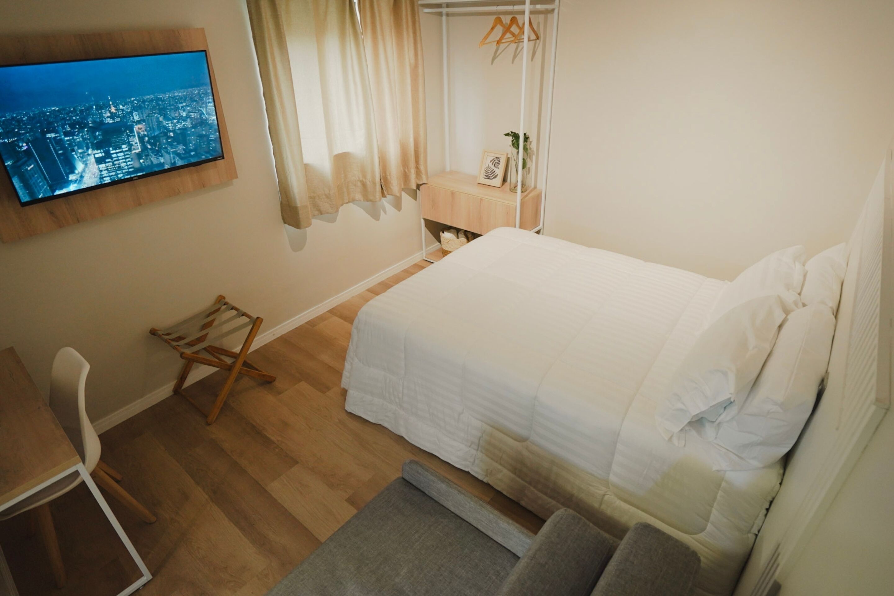 Un dormitorio ordenado con cama, escritorio y televisor montado en la pared.