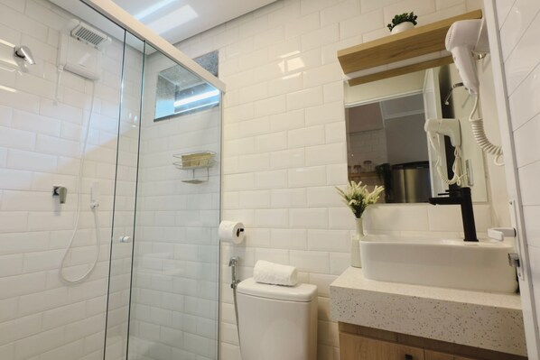 Ein modernes Badezimmer mit Duschkabine aus Glas, Toilette, Waschbecken mit Spiegel und einem an der Wand befestigten Föhn.