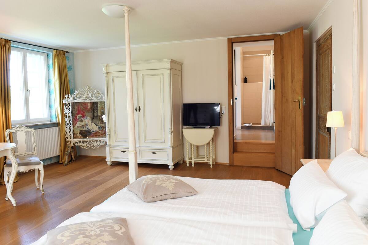 Une chambre à coucher avec un lit à baldaquin, un téléviseur posé sur une petite table, une armoire et une porte donnant sur une salle de bain.