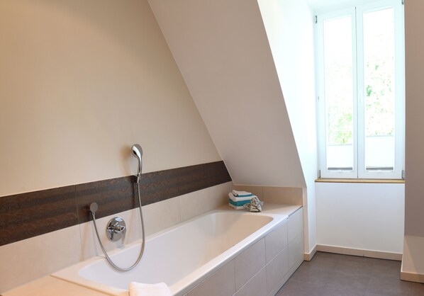 Une salle de bain moderne avec une baignoire sur pieds, une douche et une fenêtre laissant entrer la lumière naturelle.